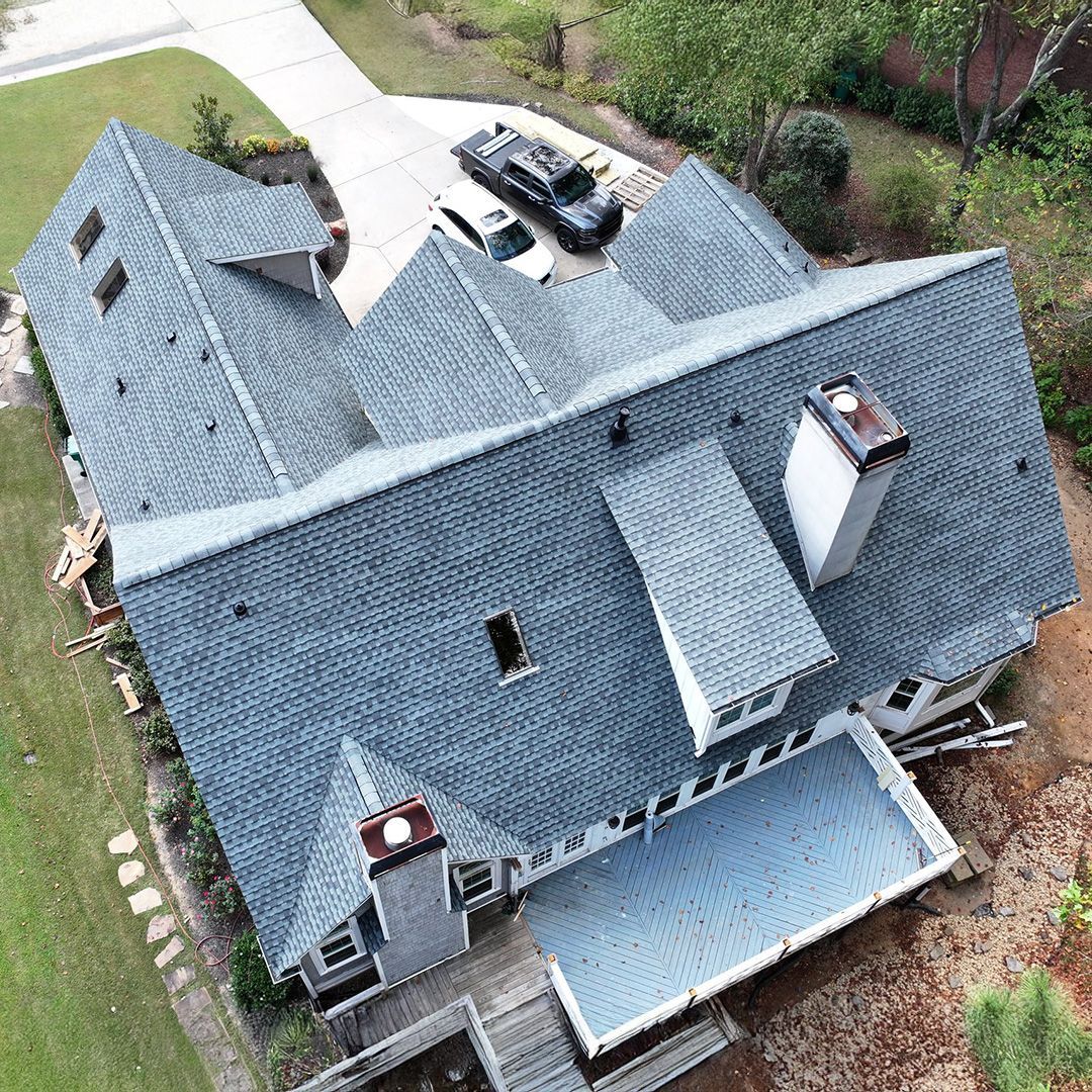 Aerial view of a gray-roofed house with skylights, a covered patio, and cars parked in the driveway.