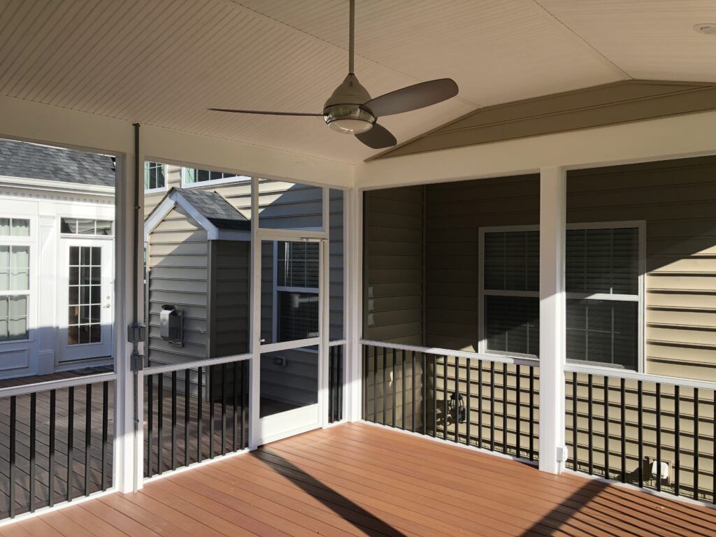 Covered wooden deck with white railing, ceiling fan, and neighboring house in the background