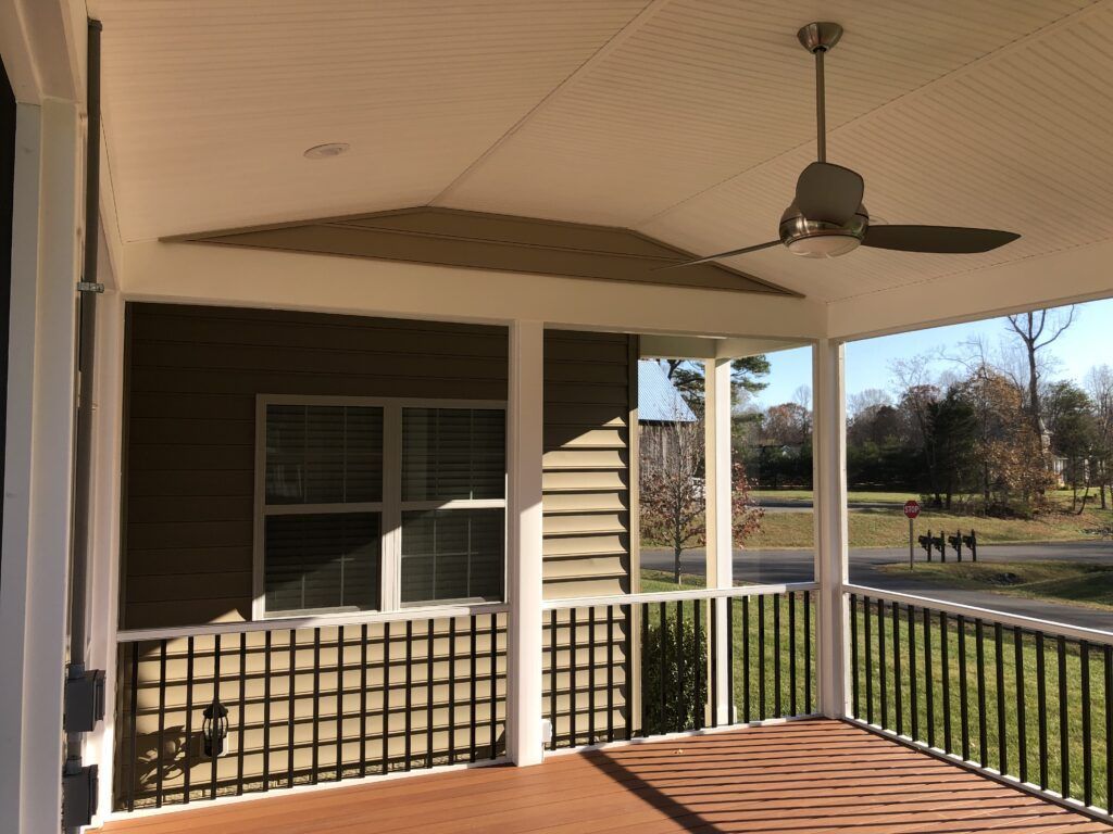 Covered front porch with ceiling fan, white columns, black railings, and a view of a yard beyond.