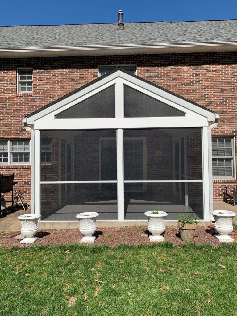 Screened porch attached to a brick house with white trim and flower planters in front