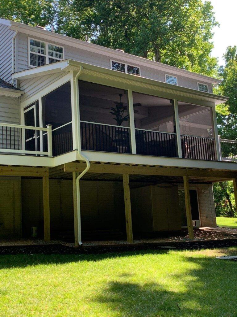 Two-story house with a screened porch and white railings, set on stilts above a grassy yard.
