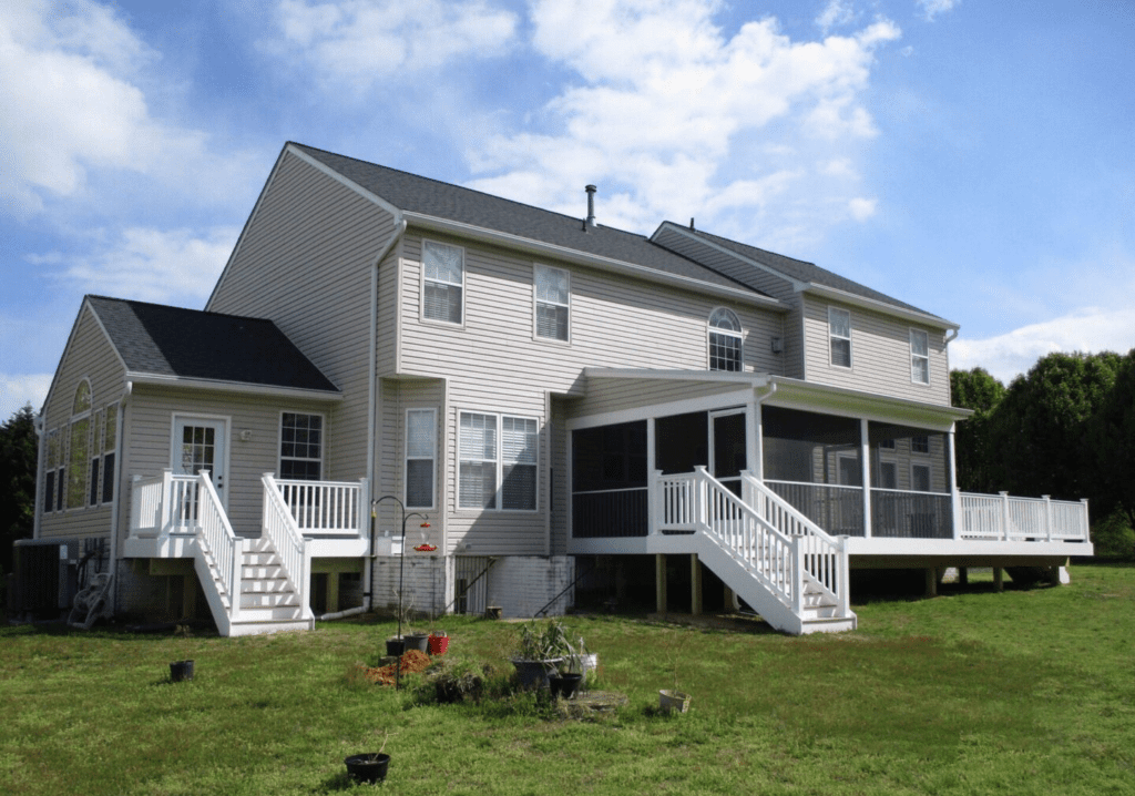 White farmhouse with porches and stairs on a grassy lawn under a blue sky