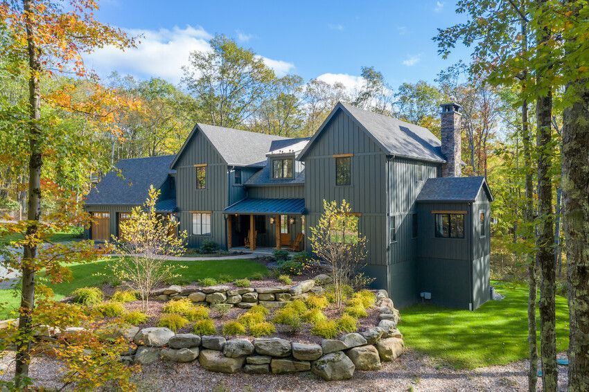 Gray modern house in a wooded autumn setting with stone landscaping and bright green lawn