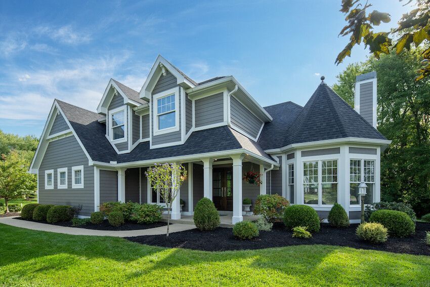 Gray suburban house with white trim, gabled roof, and a manicured green lawn under a blue sky