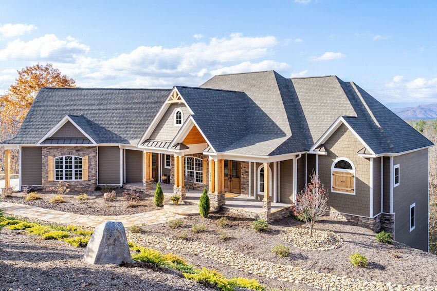 Large gray stone house with a porch and landscaped front yard under a blue sky