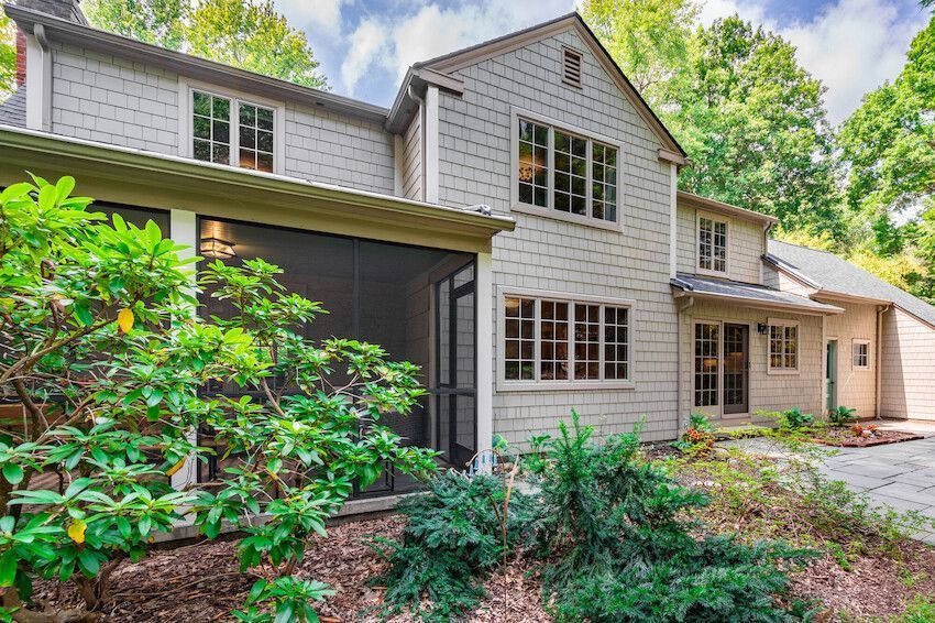 Suburban house exterior with beige siding, screened porch, and lush green landscaping