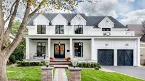 White two-story house with black trim, front porch, and double garage, viewed from the street