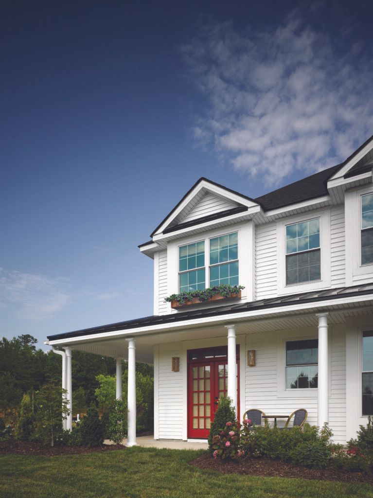 White two-story house with red front door, green shutters, and a covered porch under a blue sky