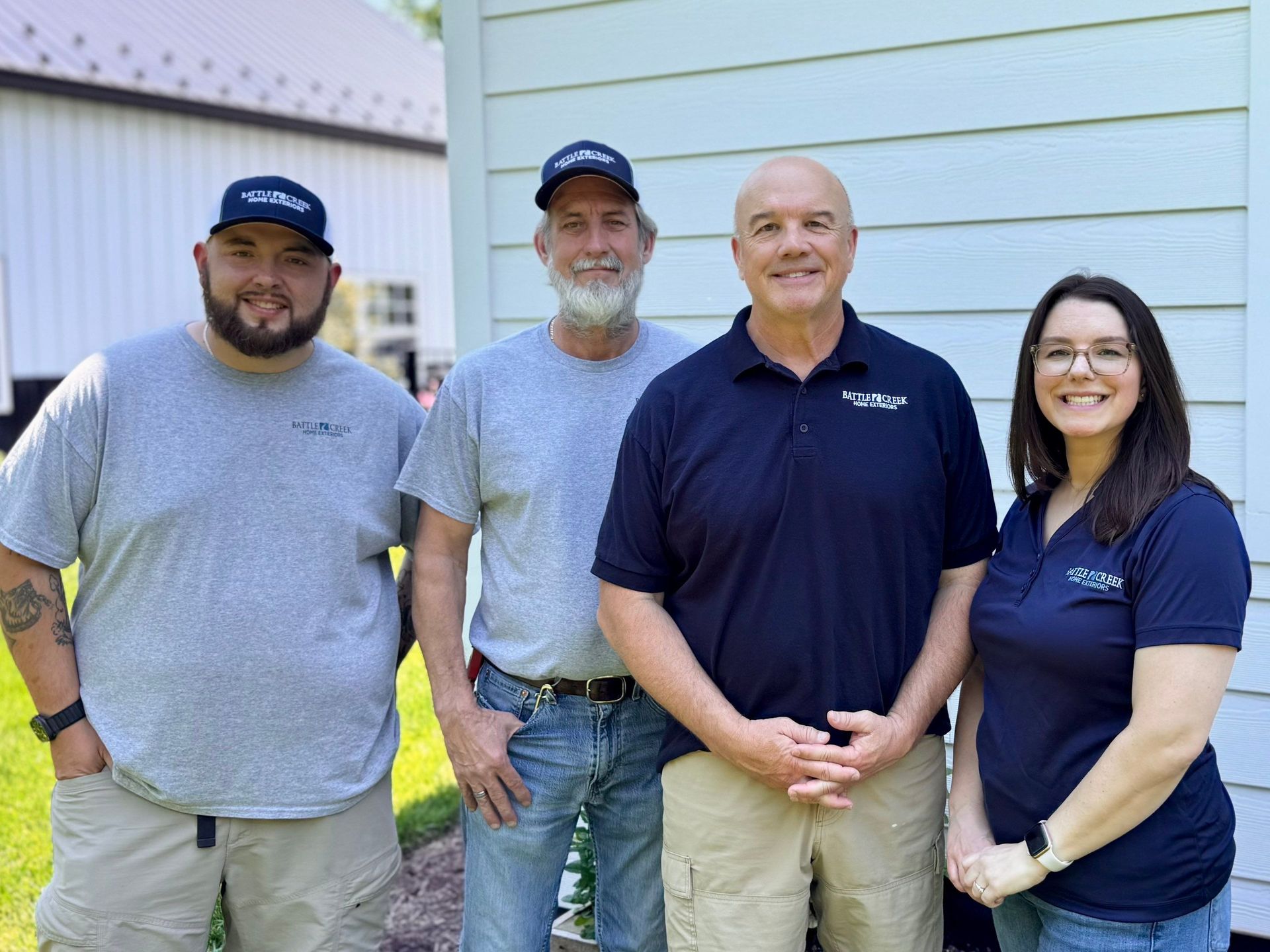 Four adults standing together outdoors in front of a house, smiling at the camera.