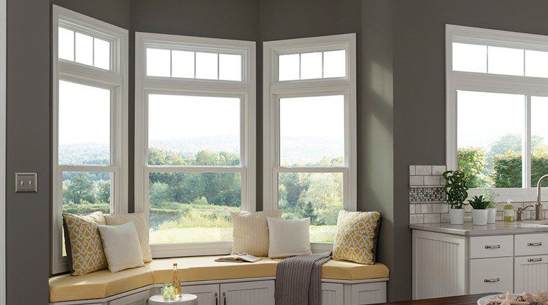 Bright window seat in a living room with cream cushions, potted plants, and a side cabinet by the window.