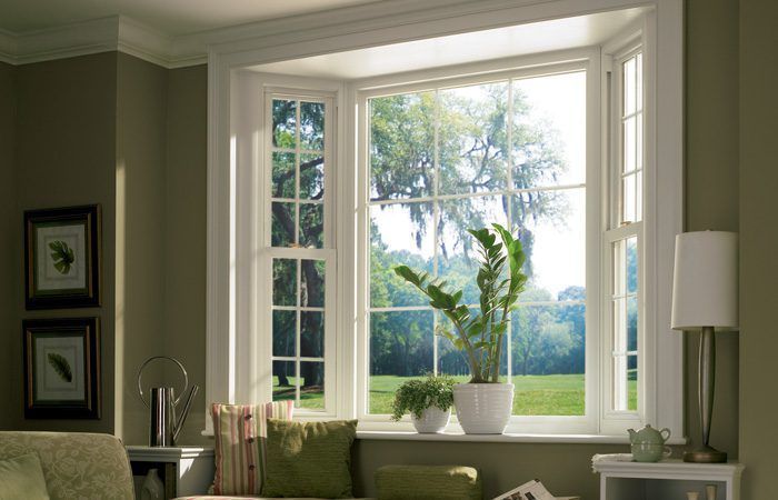 Bright living room bay window with white trim, potted plant, and framed art on soft green walls