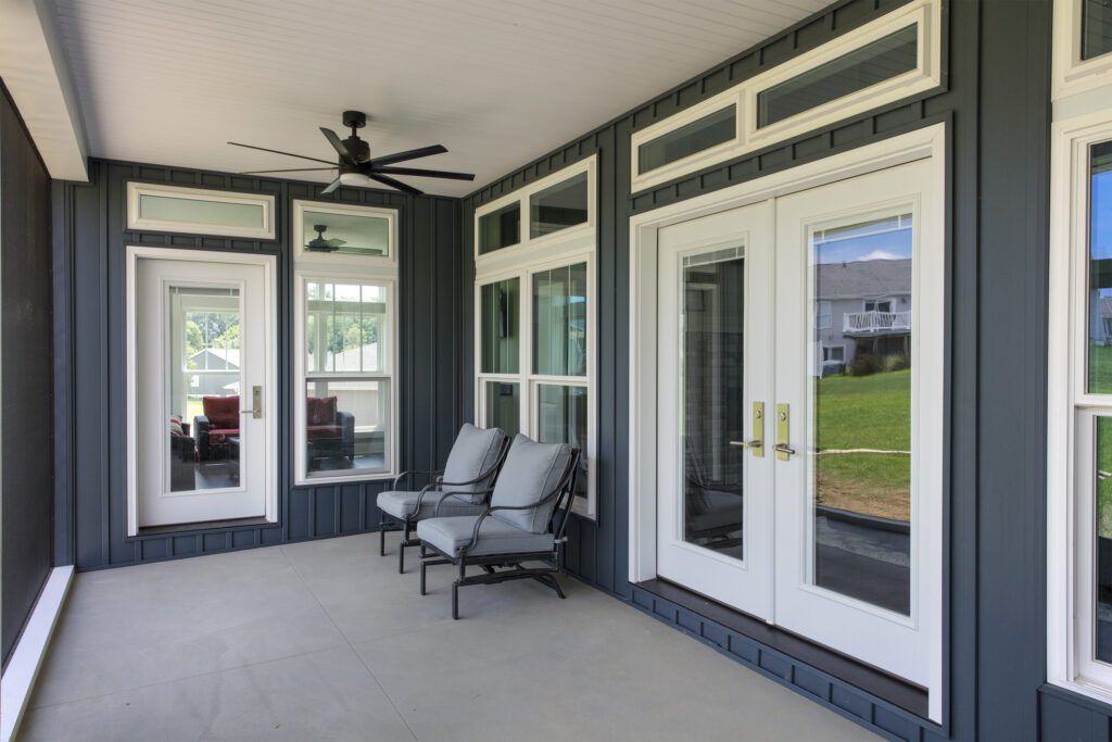 Covered porch with gray chairs, white double doors, windows, and dark blue siding