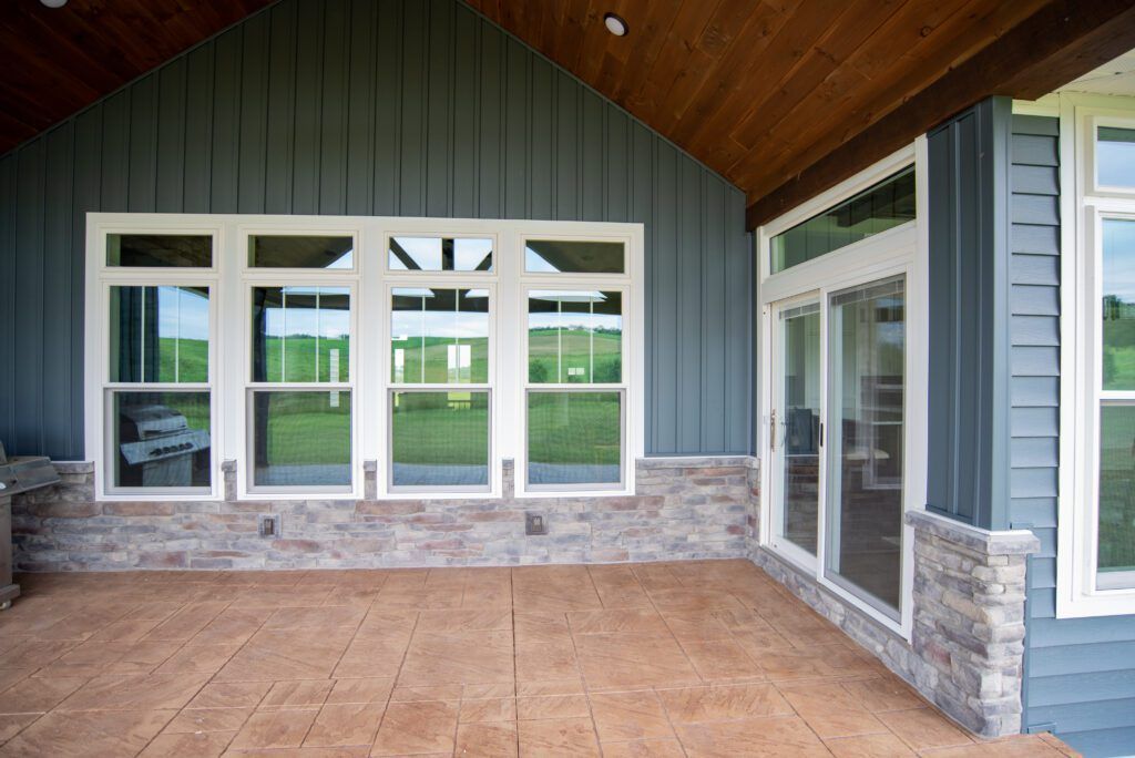 Covered patio with wood ceiling, stone base, tan tile floor, and white-framed glass doors and windows