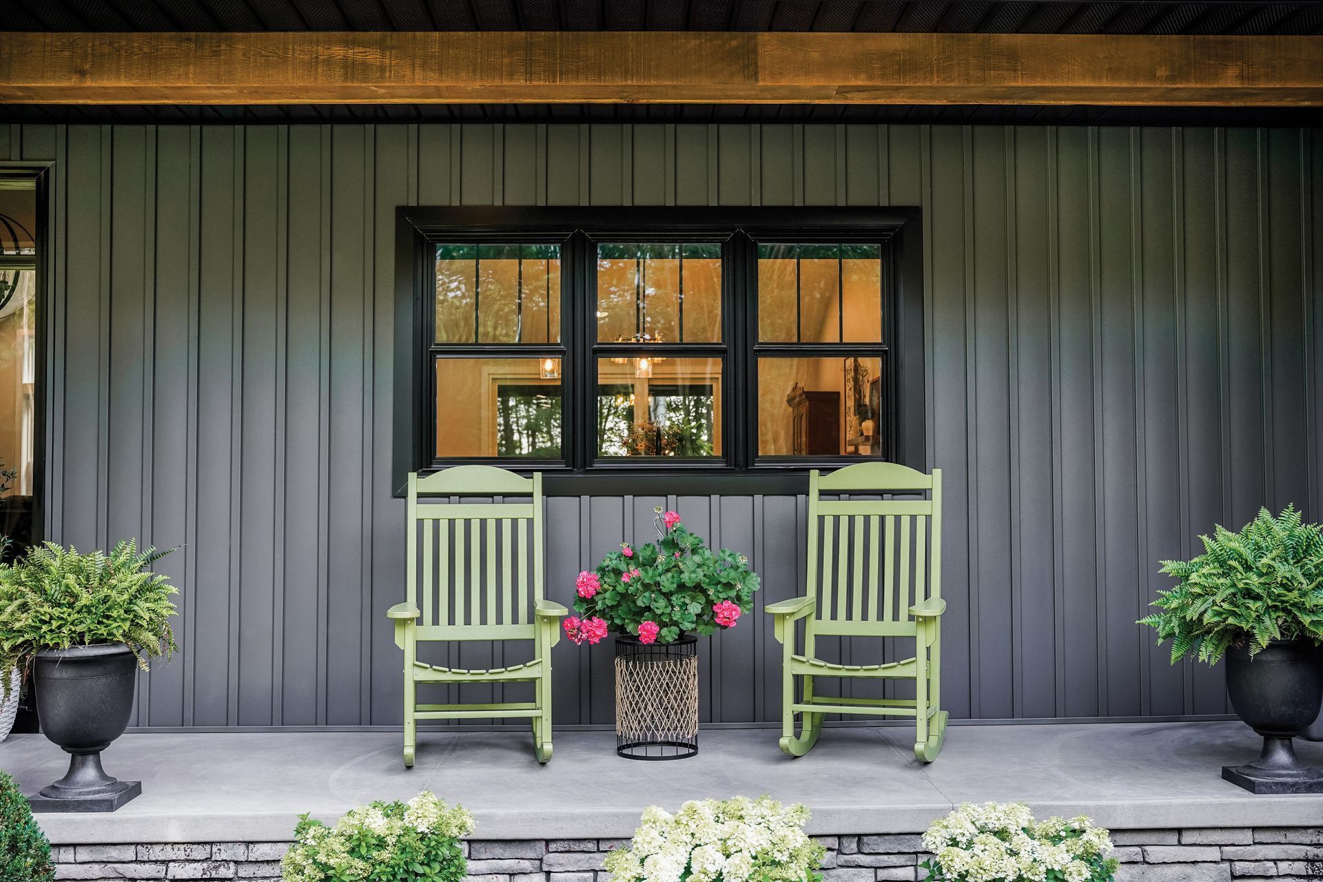 Two green rocking chairs on a porch with potted plants and a window behind them