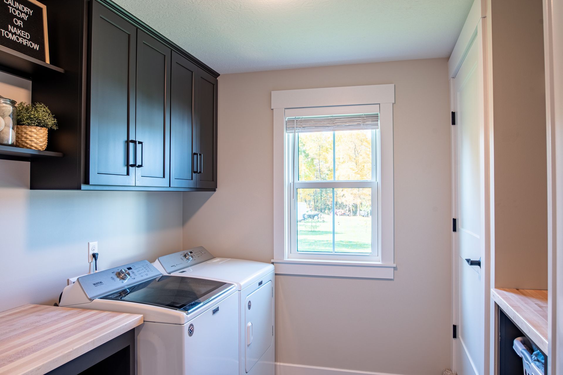 Small laundry room with white washer and dryer, dark cabinets, and a window with daylight.