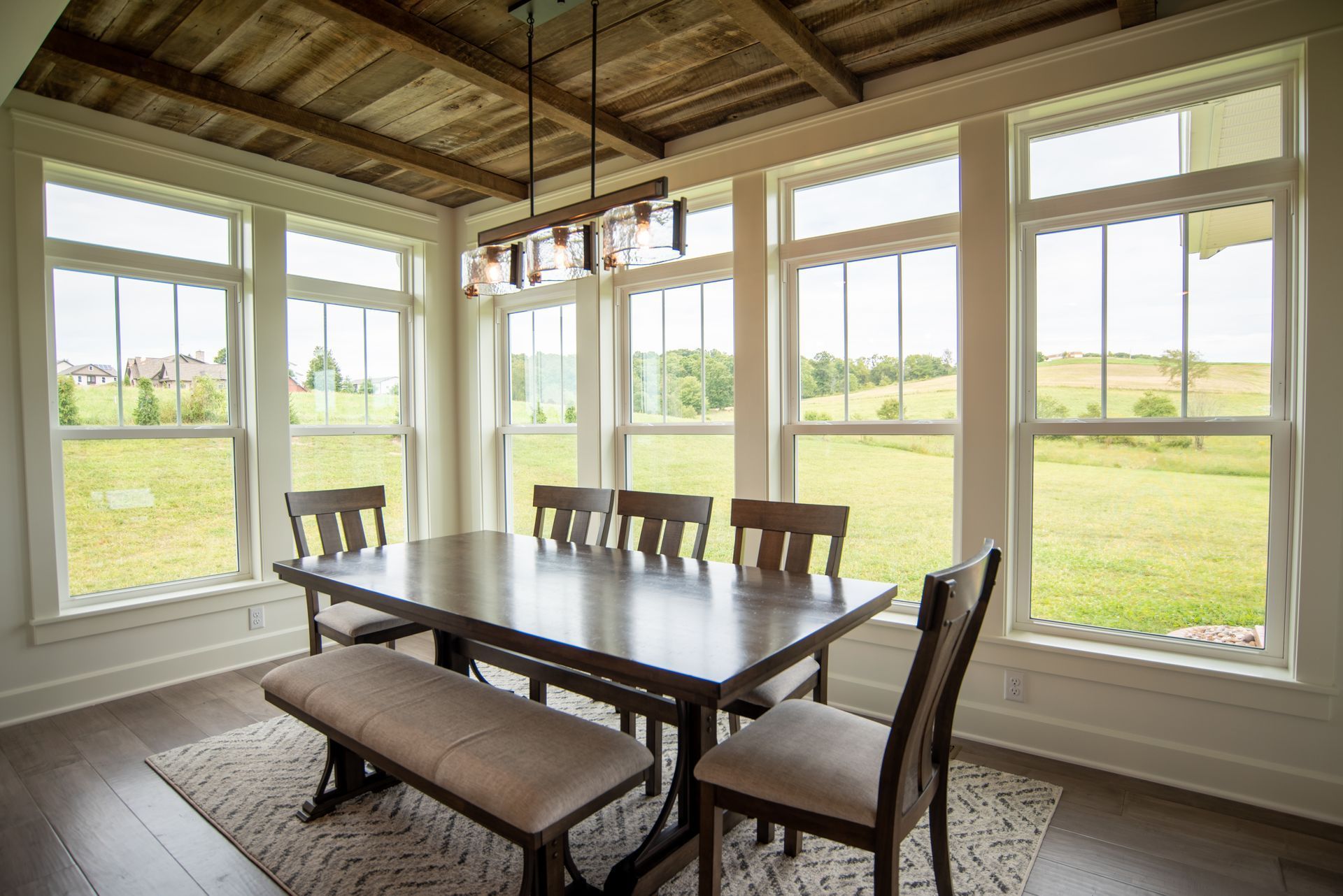 Bright sunroom dining area with a dark table, bench, and chairs overlooking green fields