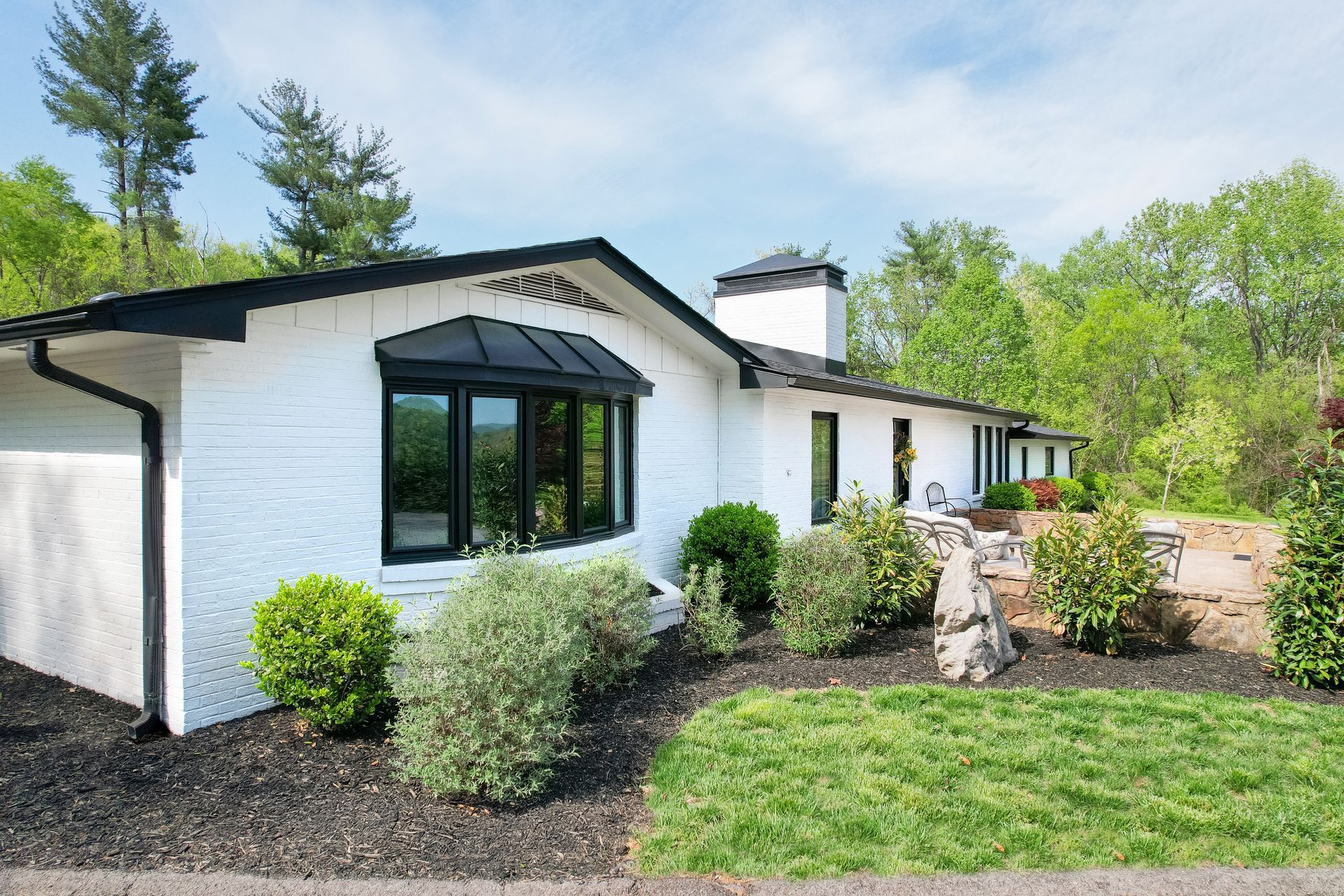 White house with black-trimmed windows, front lawn, and landscaped yard on a sunny day
