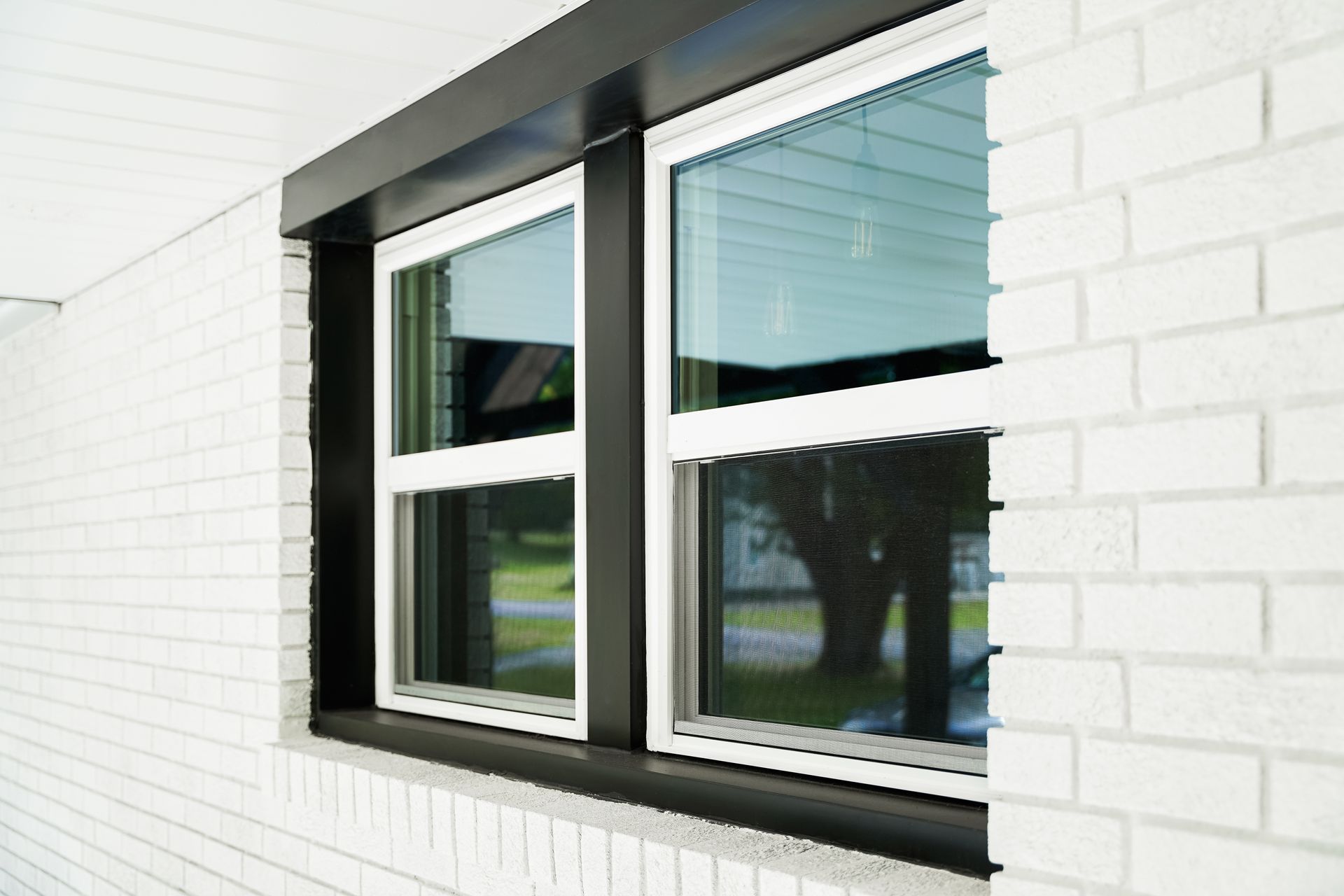 White brick wall with a black-framed window reflecting trees and greenery