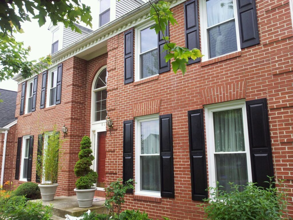 Brick townhouse with black shutters, arched entry, and potted topiary along the front walkway