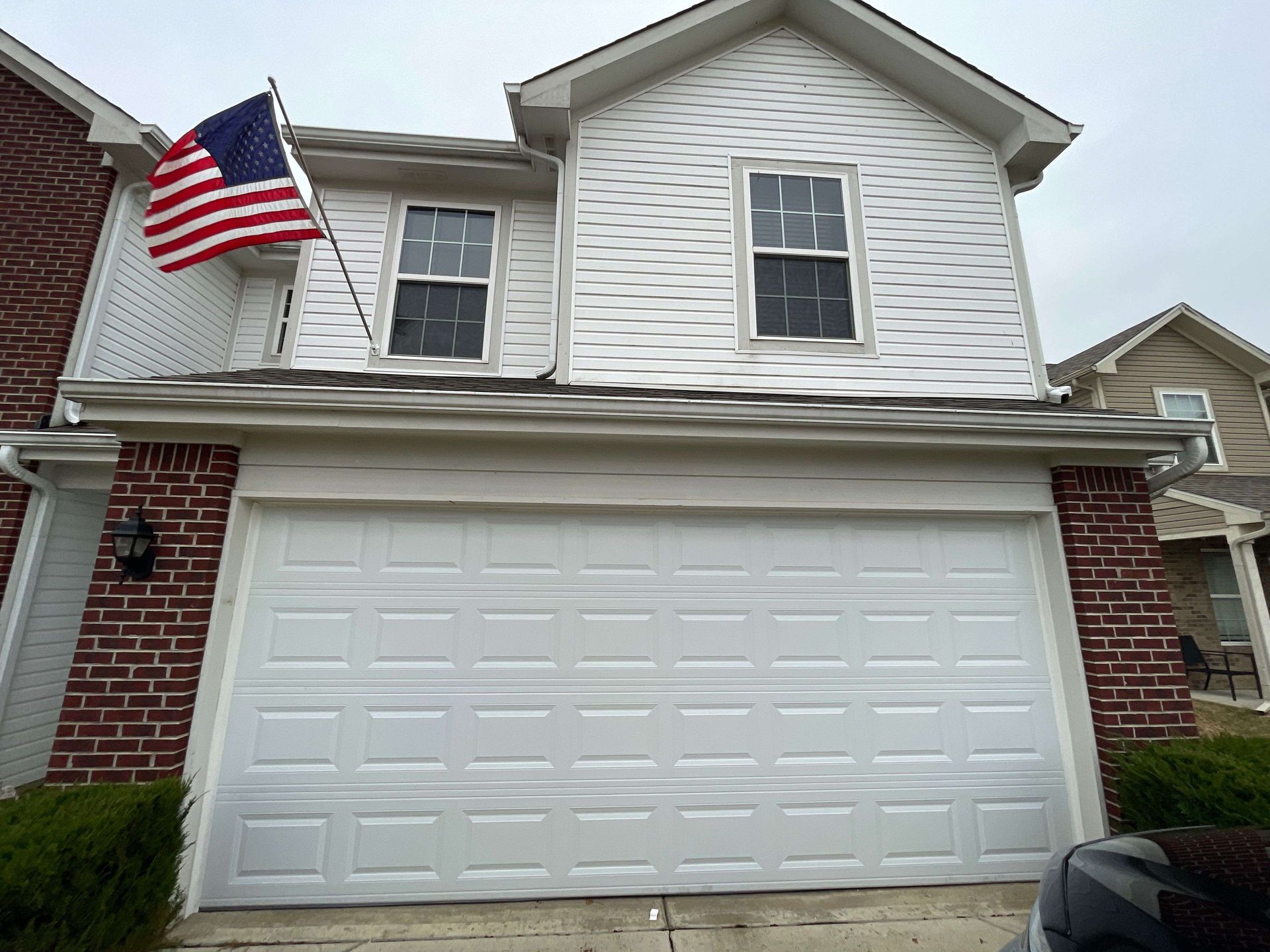 Two-story house with white siding, brick accents, a white garage, and an American flag by the front door