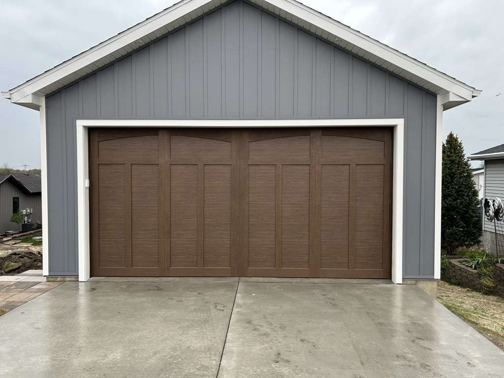 Gray garage with brown double doors and a concrete driveway at a house entrance