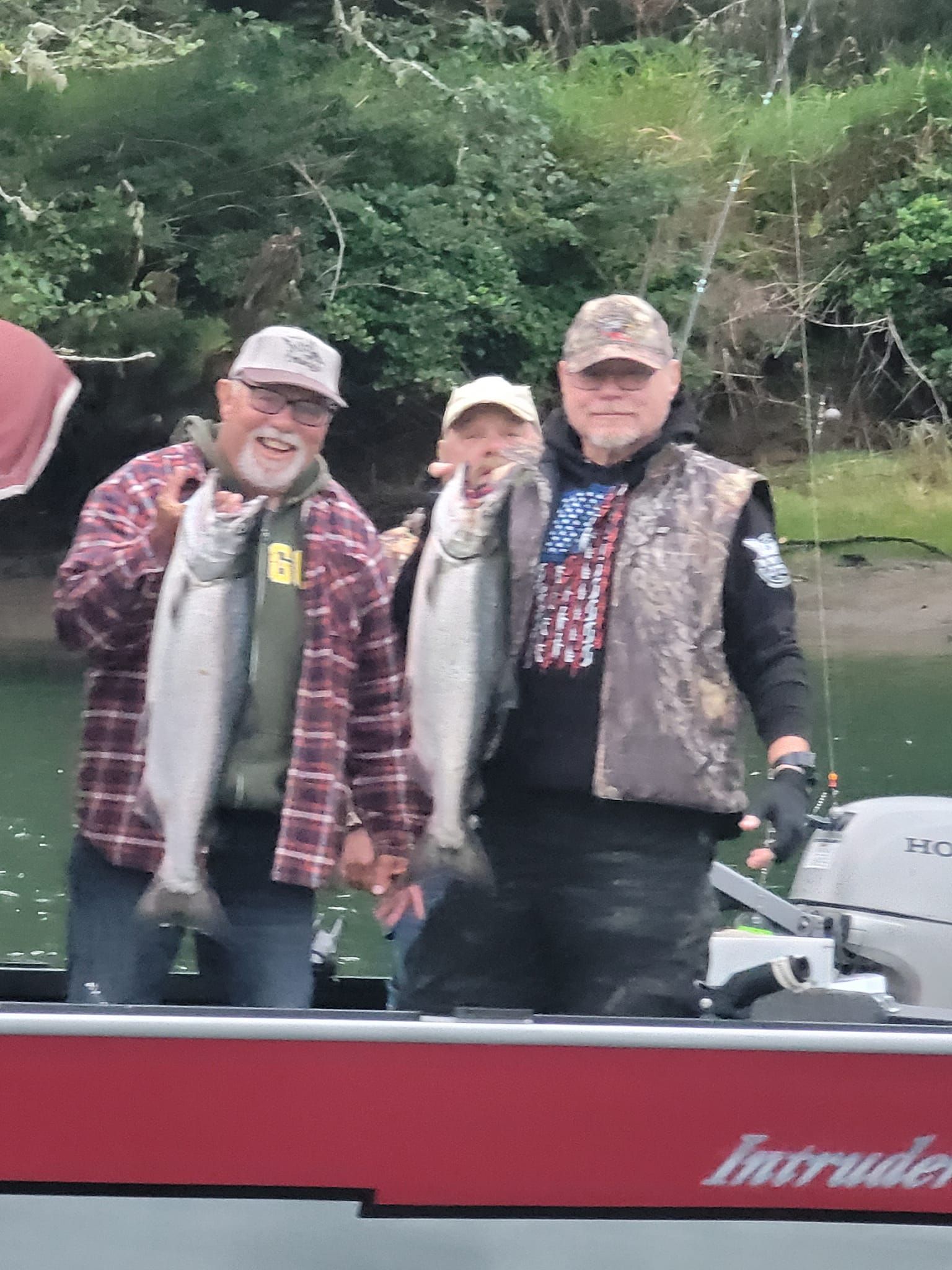 Three men are standing on a boat holding fish.