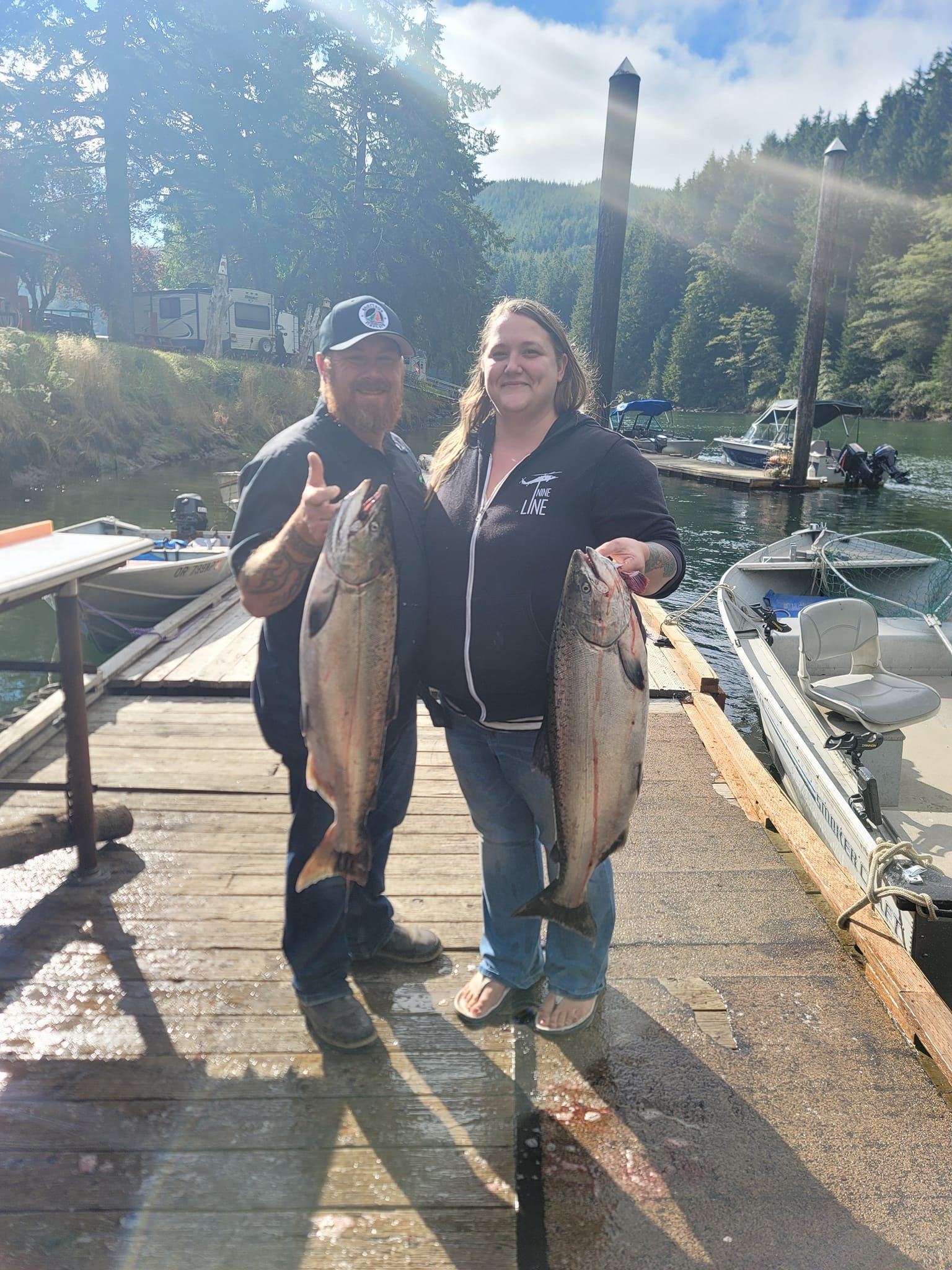 A man and a woman are holding two fish on a dock.