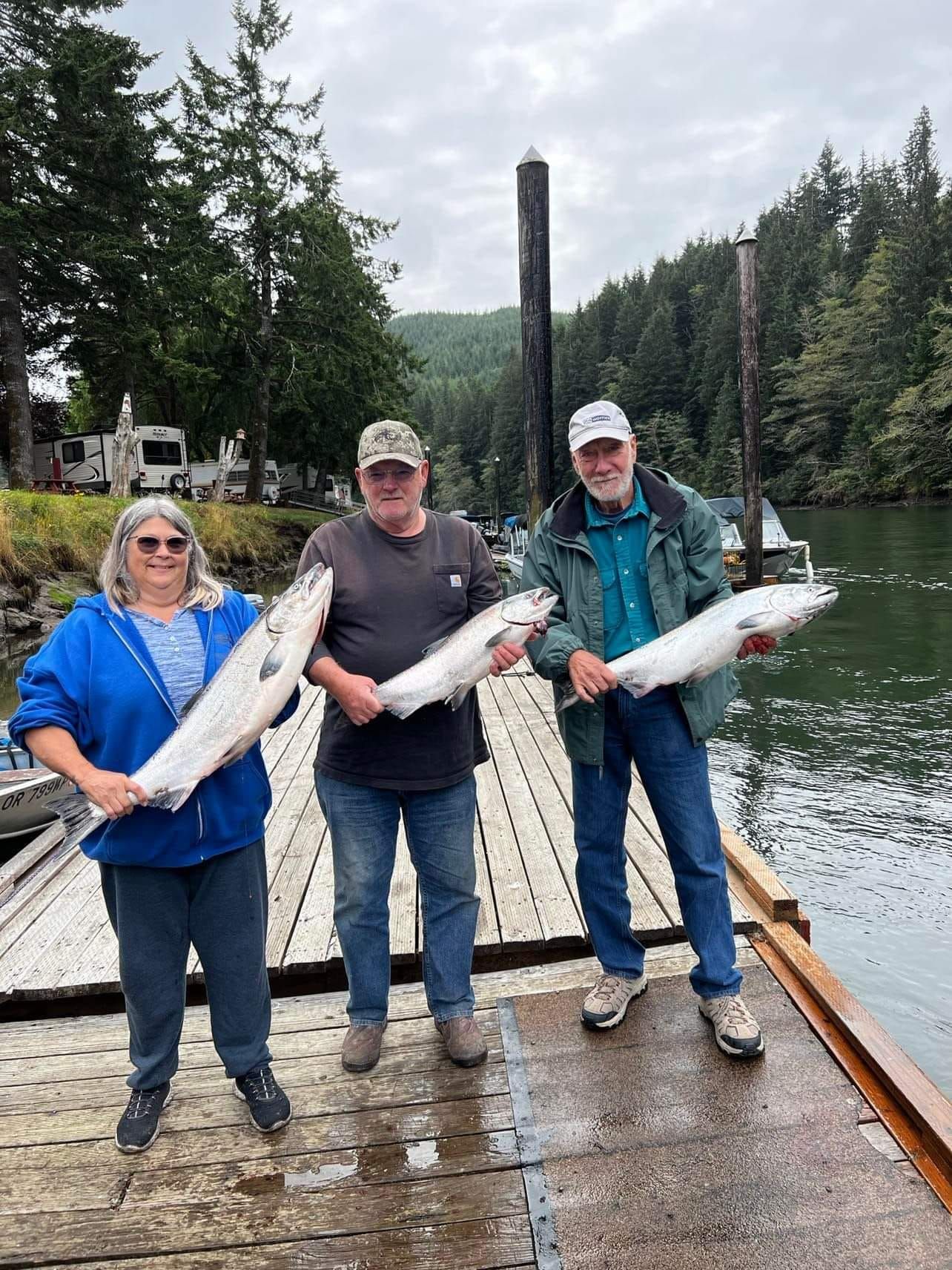 Three people are standing on a dock holding large fish.
