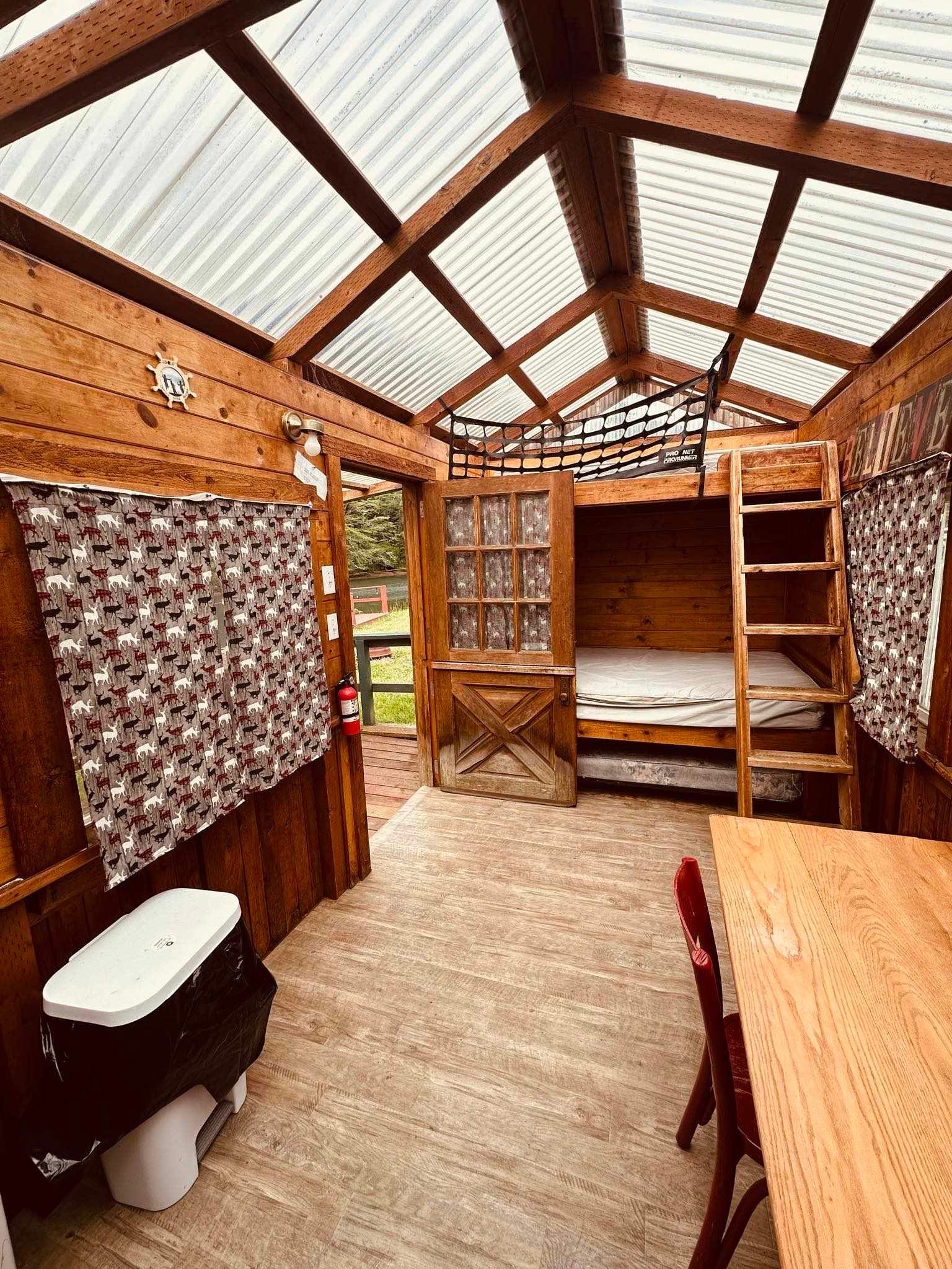 A wooden cabin with bunk beds , a table , chairs and a toilet.