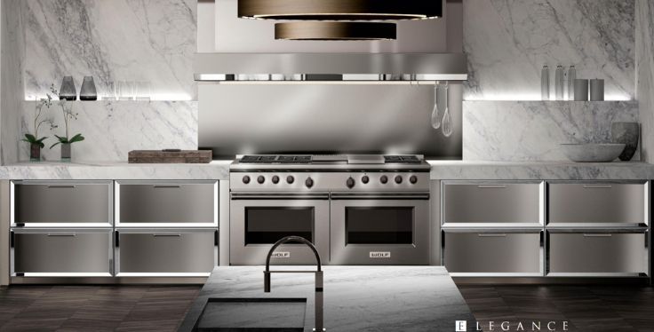 A modern kitchen with stainless steel cabinets, a professional gas range, marble backsplashes, and an island sink.