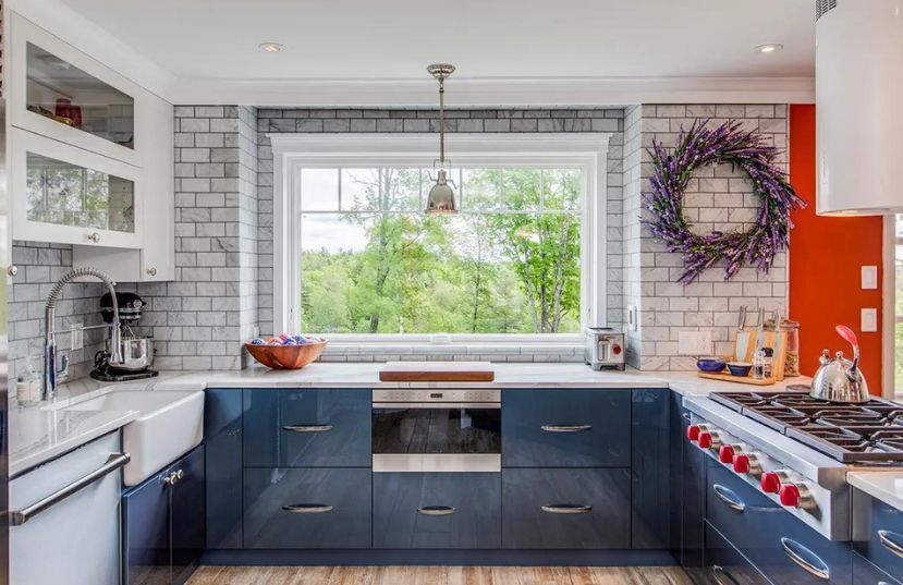 Modern kitchen with dark blue cabinets, white countertops, gray brick backsplash, and a large window above the oven.