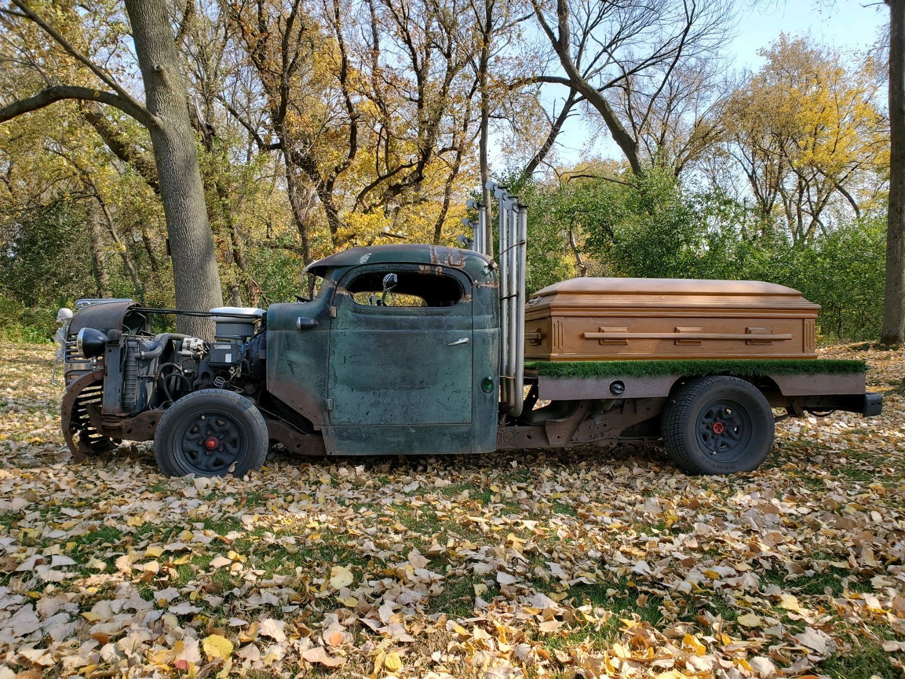 an old truck with a coffin in the back is parked in a pile of leaves