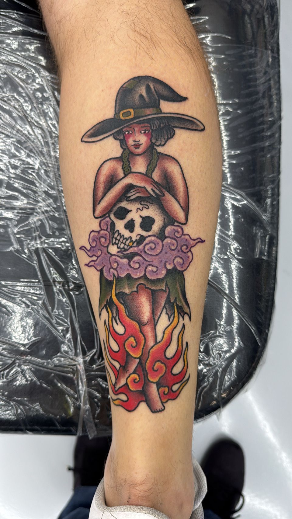 A tattoo of a witch holding a skull on a person 's leg