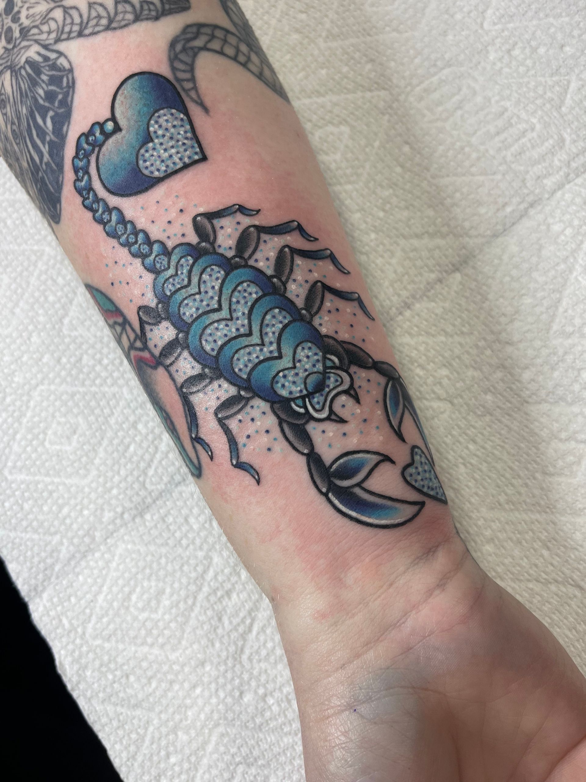 A person has a blue scorpion tattoo on their forearm