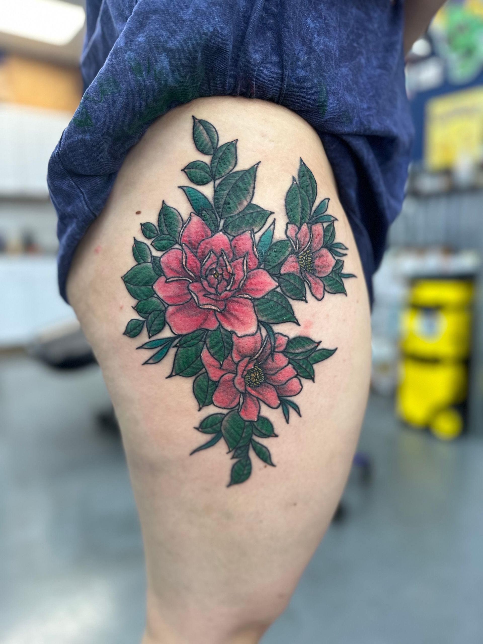 A woman has a tattoo of pink flowers and green leaves on her thigh