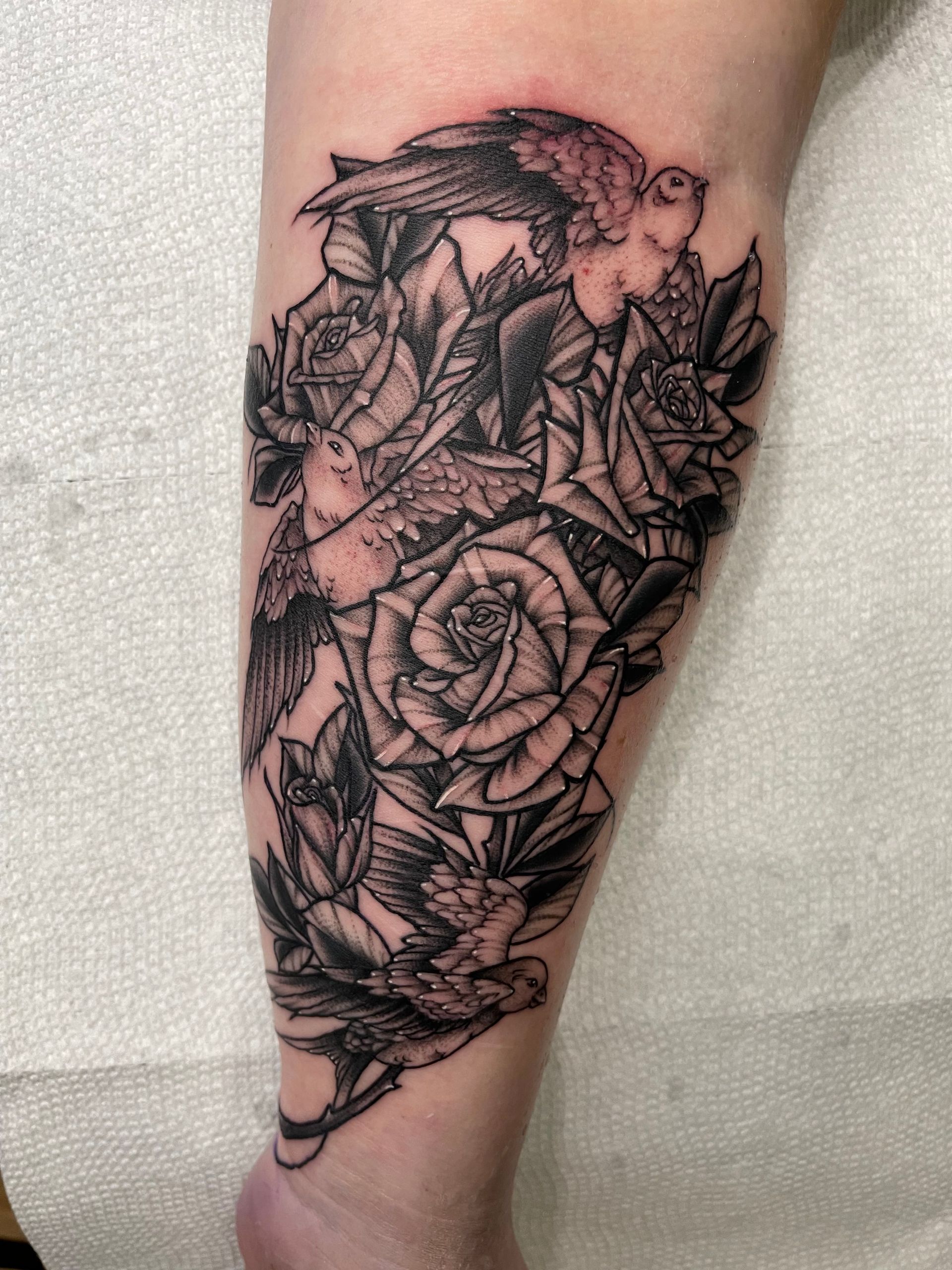 A tattoo of roses and a bird on a leg
