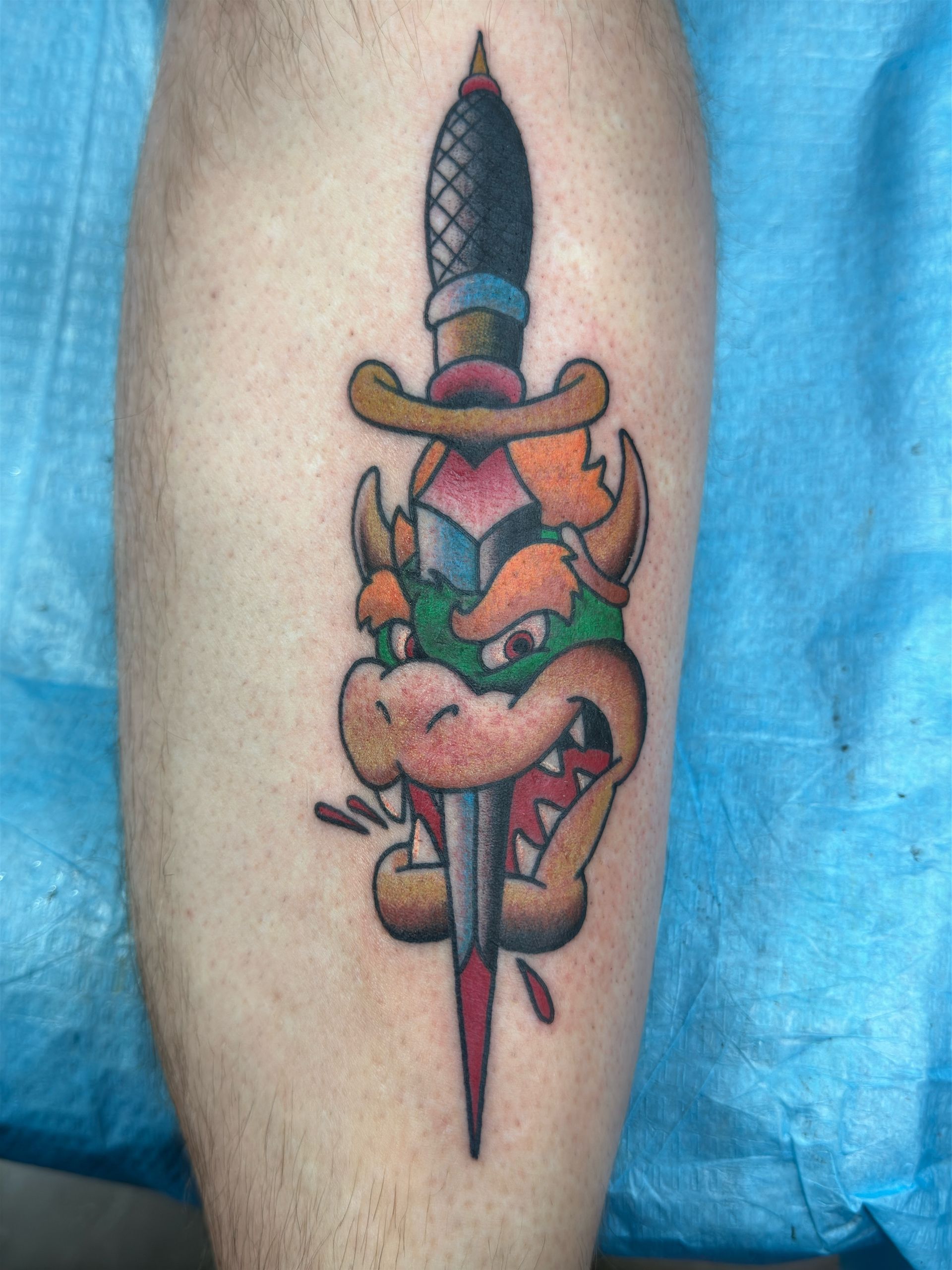 A person has a tattoo of bowser holding a dagger on their leg