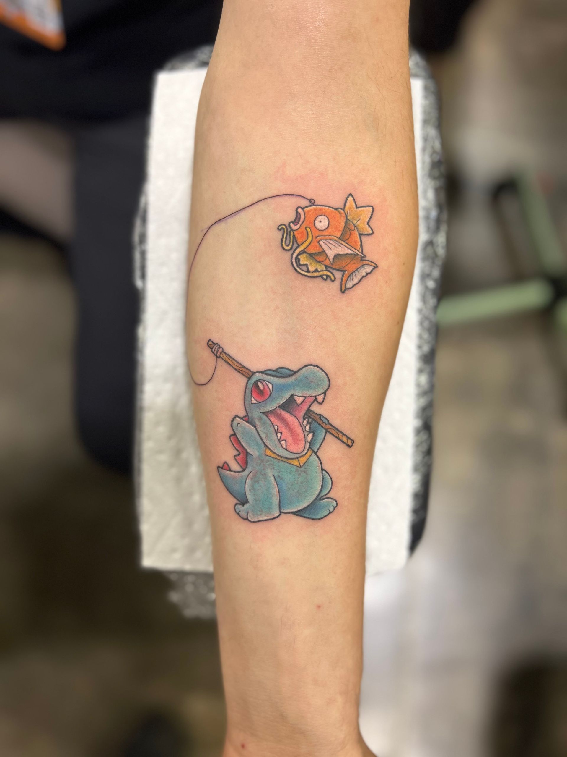 A person has a tattoo of a dinosaur fishing on their forearm