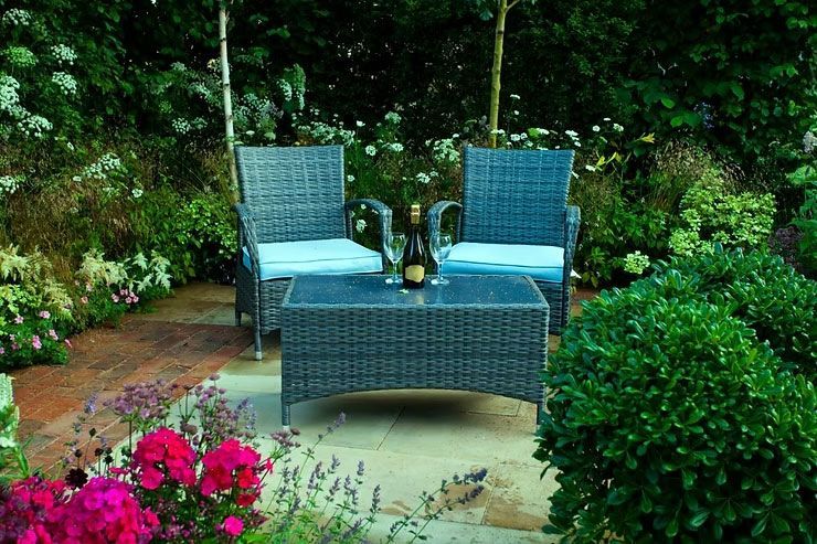 Blue wicker patio chairs around a small table in a lush garden with pink flowers.