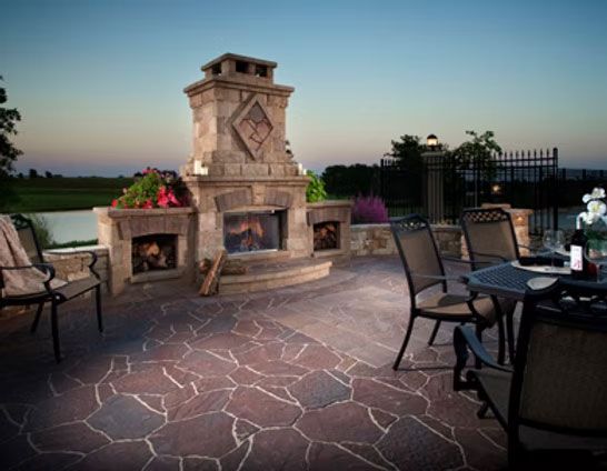 Stone patio with an outdoor fireplace and patio chairs at sunset