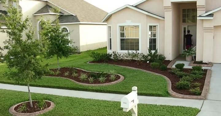 Suburban front yard with green lawn, curved flower beds, white mailbox, and beige house facade
