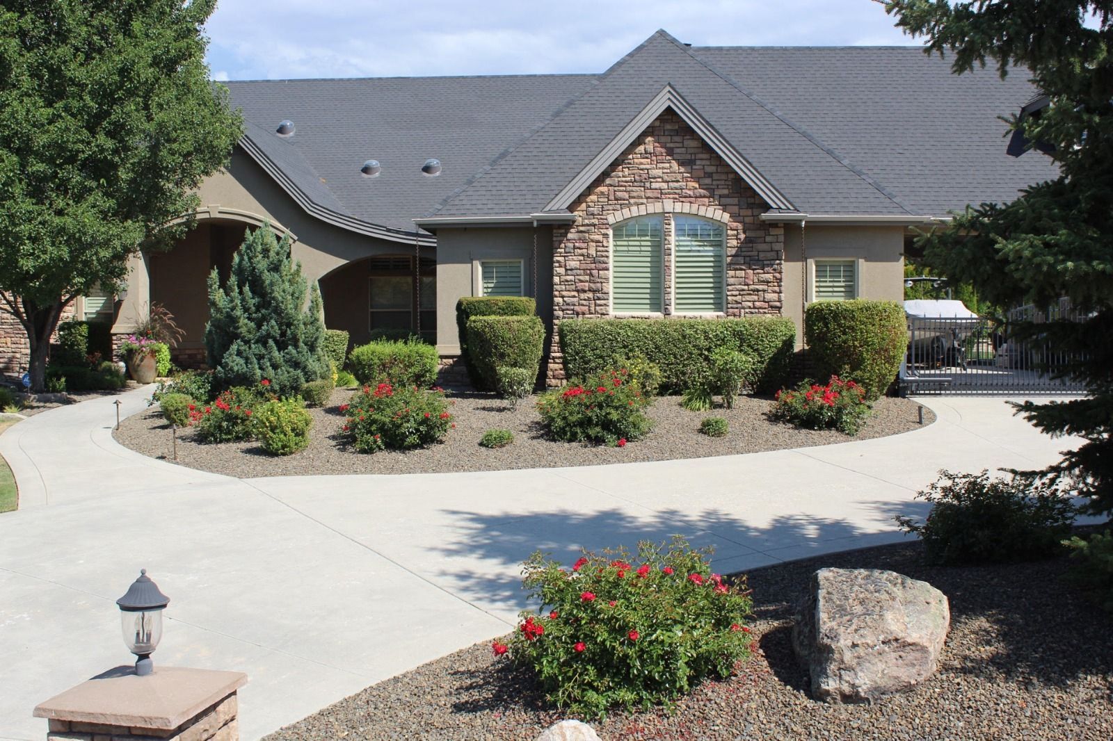 Suburban home with a stone facade, landscaped front yard, and curved driveway under a clear sky