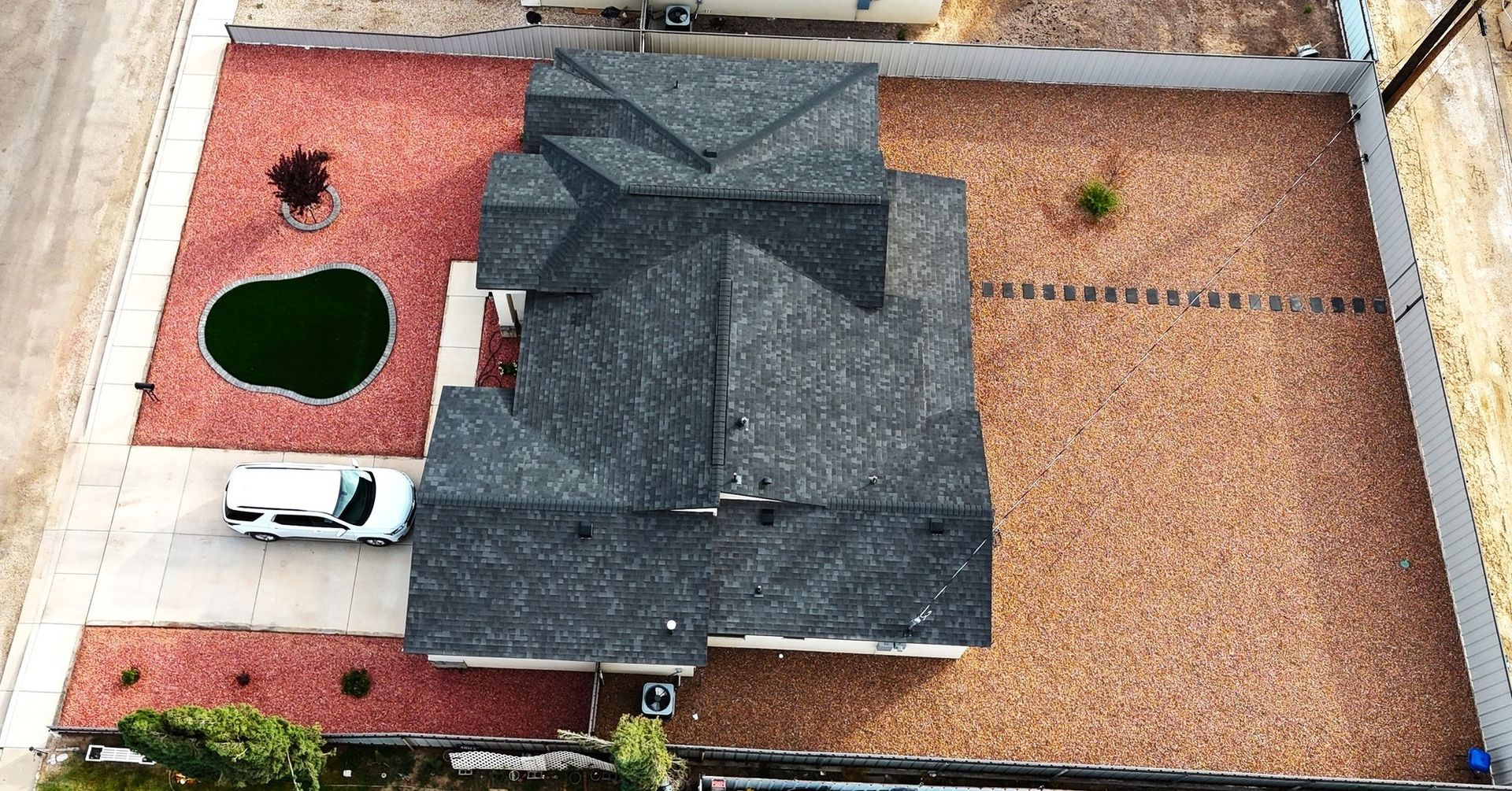 Aerial view of a house with a dark roof, red gravel yard, and a white truck parked beside it.