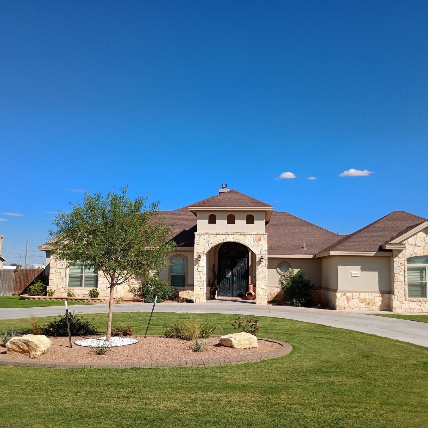 Single-story house with stone entry, arched doorway, manicured lawn, and blue sky.