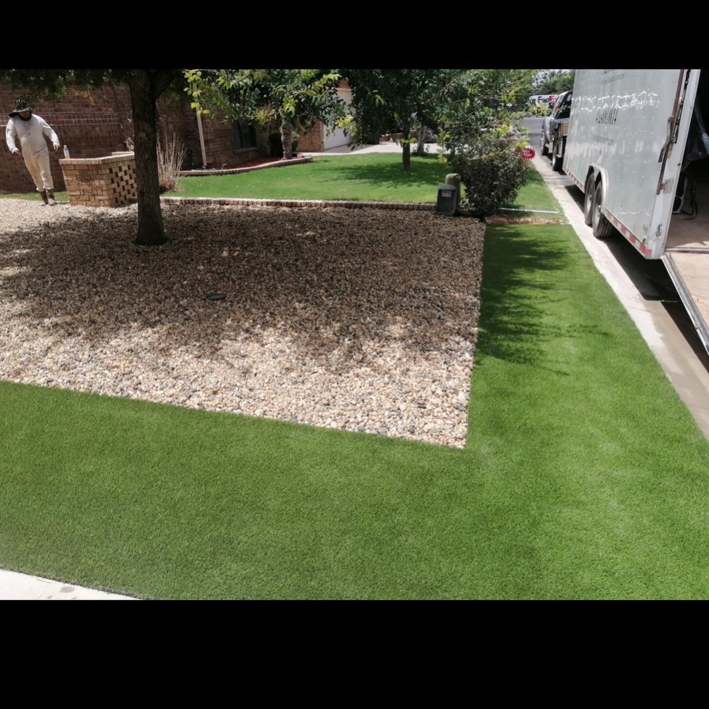 Landscaped yard with artificial grass, gravel bed, trees, and a parked truck along the curb