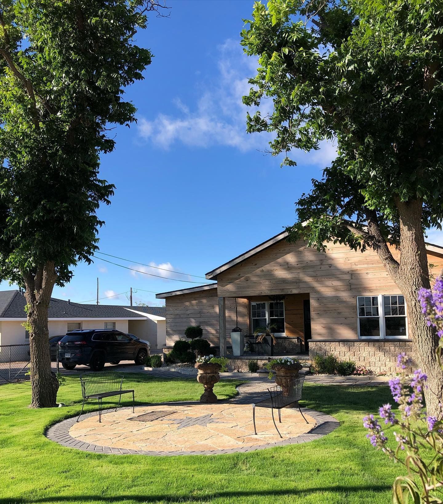 Brick house with a green lawn, circular patio, and trees under a blue sky