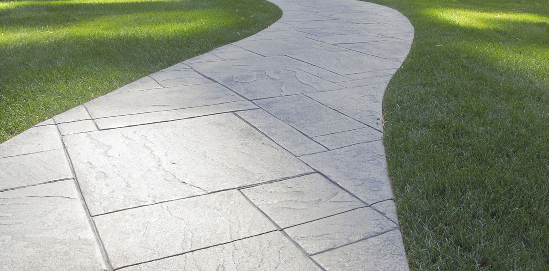 Curving light-gray stone walkway through green grass in a park