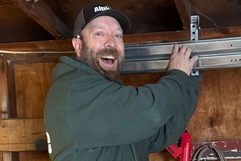Man in cap smiling, installing garage door track in a wooden garage.