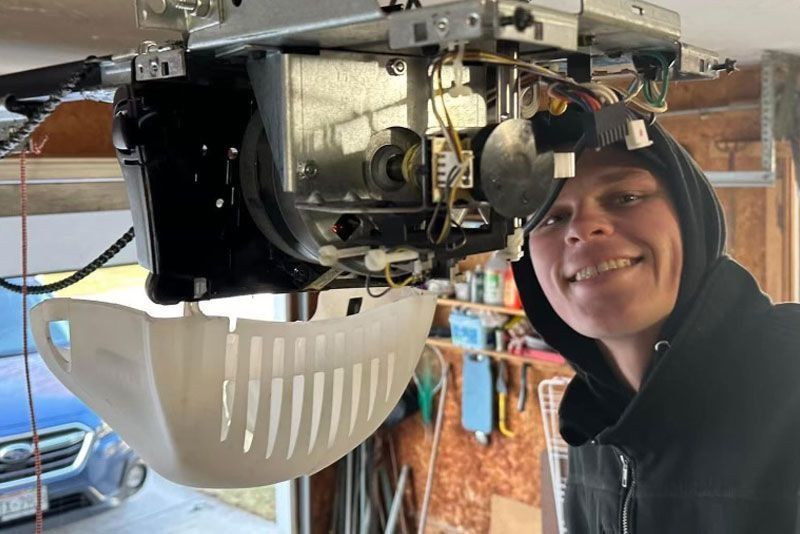 Smiling person working on garage door opener in a garage.