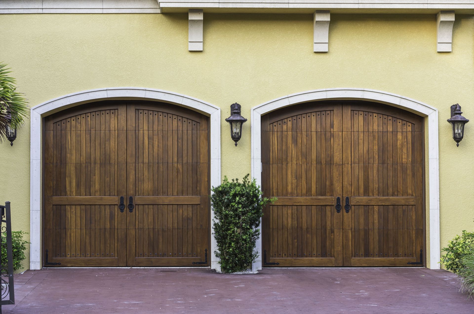 Two arched wooden garage doors with white trim on a yellow stucco exterior.